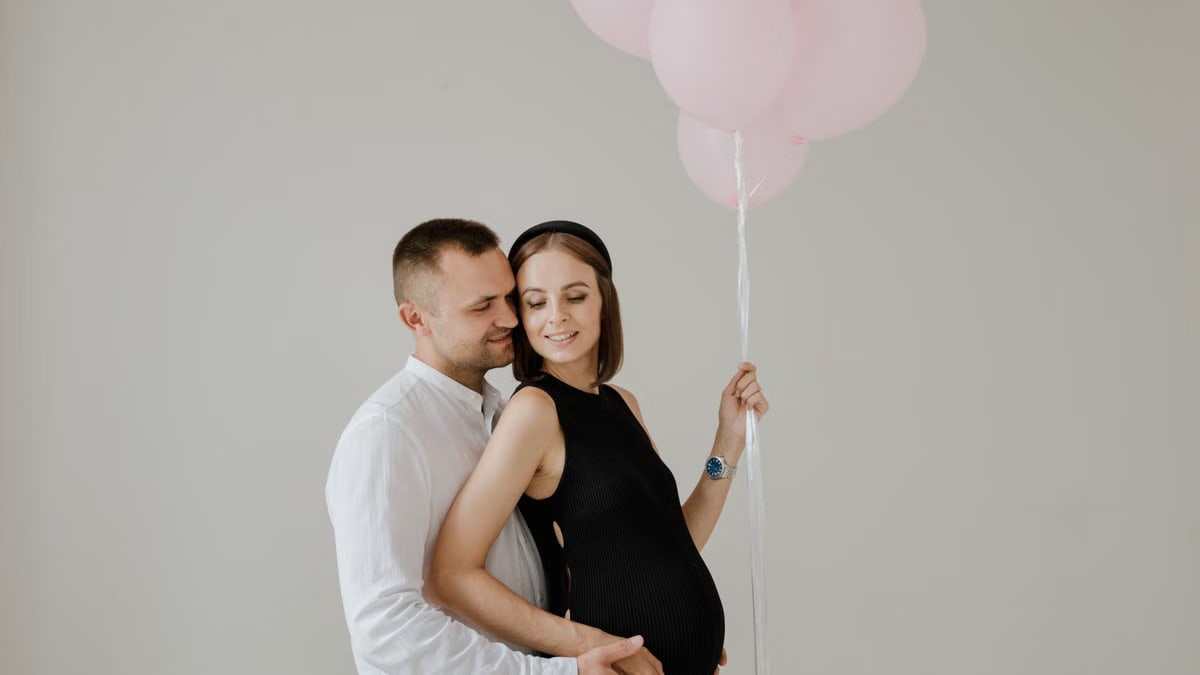 A loving couple celebrating maternity with pink balloons in a studio setting.